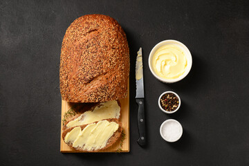 Wall Mural - Wooden board with fresh bread and bowl of butter on black background