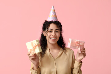 Poster - Beautiful young African-American woman in party hat with gift boxes on pink background