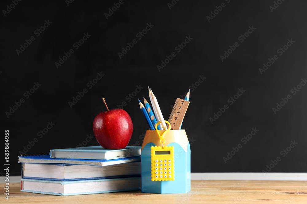 Apple, books and stationery on desk near chalkboard. Back to school concept