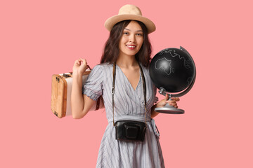 Wall Mural - Young Asian woman with globe and suitcase on pink background. Travel concept