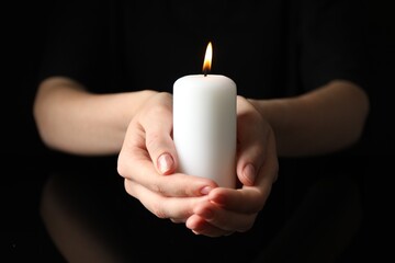 Wall Mural - Woman holding burning candle on black background, closeup