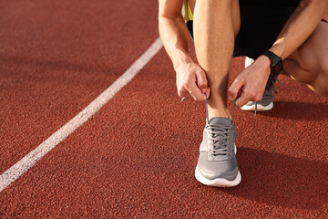 Wall Mural - Man tying shoelace of grey sneaker at stadium, closeup. Space for text