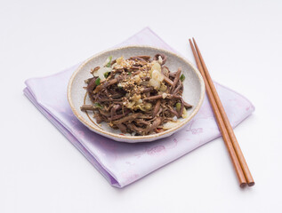 Sticker - Close up of seasoned bracken with sesame seeds and onion on ceramic dish and pink cloth with wooden chopsticks, South Korea
