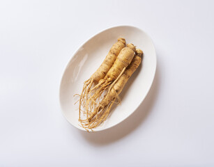 Poster - Close up and top angle view of three raw ginseng roots with soil on dish and white floor, South Korea
