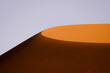 © Massi Arezki - A sunlit sand dune stands out against a clear sky, capturing the minimalist beauty and striking contrasts of the Namibian desert landscape.