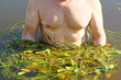 © FEDOR - one strong naked man stands in dirty water in a swamp among green organic long living algae during the day in summer