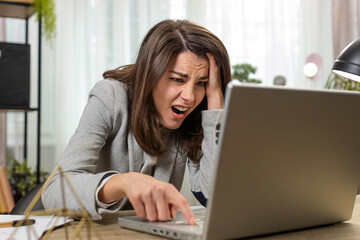 Upset business woman programmer software developer in formal suit working on laptop loses system error virus bad news fortune data loss fail at home office table. Sad young female freelancer girl