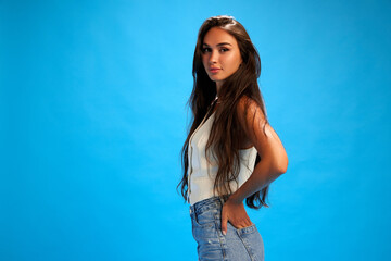 Side view portrait of young woman in casual attire looking at camera against blue studio background. Trendy colors. Concept of human emotions, fashion and style, business.