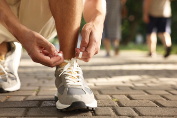 Wall Mural - Man tying shoelace of grey sneaker outdoors, closeup. Space for text