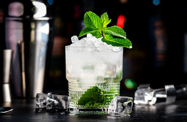 Wall Mural - Gin cocktail drink with lime juice, syrup, soda, fresh mint and crushed ice. Black bar counter background