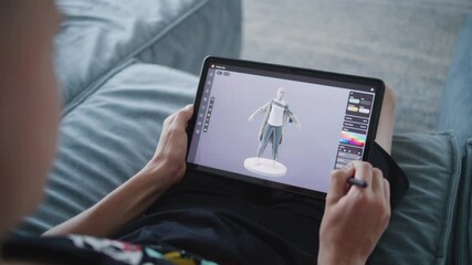 Fototapete - Focused teenager draws clothes for game character using 3d modeling program. Boy with digital pencil and tablet in hands sits in room, creates 3d models. Game design and development concept. Close up.