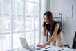 © Wasana - A woman is talking on her cell phone while sitting at a desk with a laptop