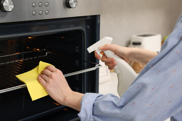 Poster - Woman cleaning oven rack with rag and detergent in kitchen, closeup