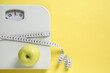 © New Africa - Scale tied with measuring tape and fresh apple on yellow background, top view. Space for text