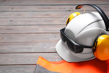 Wall Mural - Reflective vest, hard hat, earmuffs and goggles on wooden background, space for text