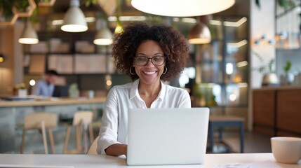 Wall Mural - Smiling woman with glasses working on laptop in modern office space with contemporary decor and background activity