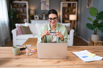 Young business woman using break from working in home office for paying home finances or online shopping with credit card and laptop computer. Confident female pay her online order.