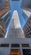 © lililia - A low angle view of several skyscrapers in a city, seen from the ground. The buildings are lit up with windows, and the sky is a pale blue color