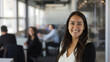 © VK Studio - A smiling woman standing confidently in a modern office, exuding warmth and friendliness, with colleagues working in the background.