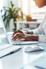 Close-up of hands typing on a laptop keyboard in a bright office.
