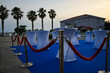 © juraj - Vip area is set up outside for an event with white cocktail tables, red velvet ropes, and a blue carpet