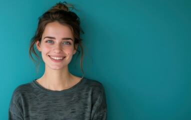 Canvas Print - A young woman with brown hair tied up in a bun smiles at the camera while standing in front of a teal wall