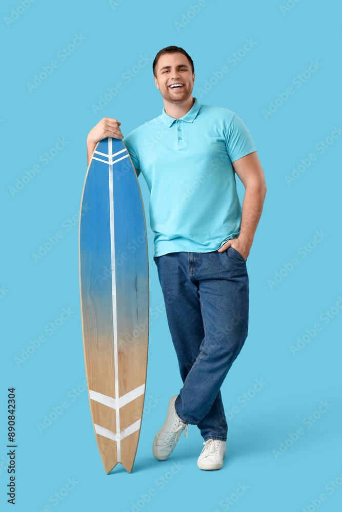 Happy young man with wooden surfboard on blue background