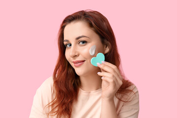 Sticker - Beautiful young woman with heart-shaped makeup sponge on pink background