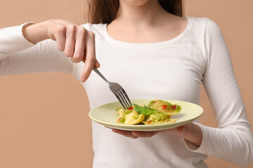 Young woman holding plate of tasty ravioli on brown background, closeup