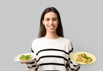 Beautiful young woman with plates of tasty ravioli on grey background