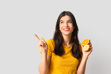 Poster - Beautiful young woman with citrus fruits pointing at something on grey background