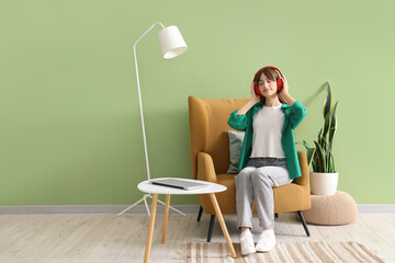 Sticker - Young woman with headphones sitting in armchair near green wall