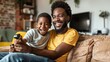 © Damerfie - A delighted father and his son are seated on a sofa in their cozy living room, sharing laughter and bonding over playing video games with a controller in hand.