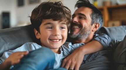 Wall Mural - A father and his young son are captured sharing a joyful moment on a cozy sofa, both smiling and enjoying a precious bonding time in the warmly lit ambiance of their home.