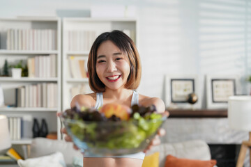 portrait attractive young woman in sportswear holding bowl of fresh vegetable standing in the living room after exercise,concept of healthy lifestyle,health care,vegetarian diet,loss weight