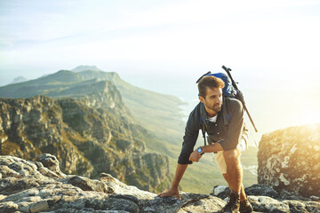 Canvas Print - Thinking, climbing and man on mountain with sunset, achievement and rocks on holiday adventure. Nature, inspiration and hiker on cliff with backpack, hiking and trekking on outdoor vacation.