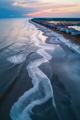 Wall Mural - A long wave is crashing on the shore of a beach. The beach is lined with houses and a pier. The sky is a beautiful mix of blue and orange hues