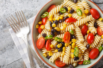 Sticker - simple hearty salad of fusilli pasta, black beans, tomato and corn close-up in a plate on the table. Horizontal top view from above