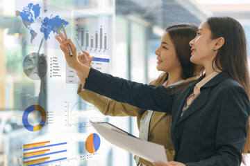 Wall Mural - Two Young Asian businesswomen discuss a new startup project Idea presentation and analyze planning, financial statistics, and investment market at the office.