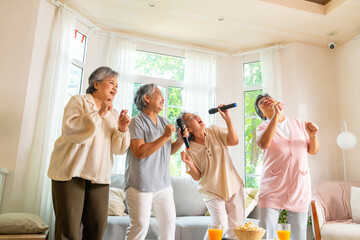 Group of Happy Asian senior women friends singing karaoke with dancing together in living room. Elderly retired people enjoy and fun indoor lifestyle spending time together with home entertainment.