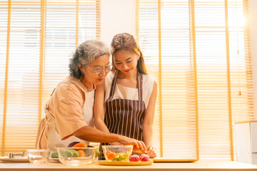 Happy Asian family enjoy and fun indoor healthy lifestyle cooking and having dinner together at home. Senior mature mother teaching adult daughter making vegan food vegetables salad in the kitchen