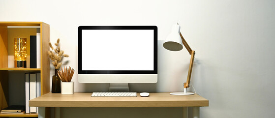 Wall Mural - Front view of blank screen computer desktop, lamp and books on wooden table against white wall