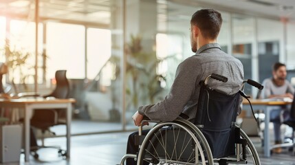 Aufkleber - Man in a wheelchair facing away, working in a bright open office. Emphasizing accessibility and employment opportunities for disabled professionals.
