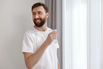 Sticker - Happy young man with glass of water near window at morning