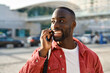 © insta_photos - Happy young African Black man hipster or tourist with backpack standing on city street outdoors holding smartphone talking on mobile cell phone having conversation making call on smartphone.