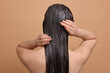 © New Africa - Woman applying hair mask on beige background, back view