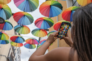 Woman taking pictures of colorful umbrellas with her smartphone. Woman taking pictures of colorful umbrellas with her smartphone in a decorated street