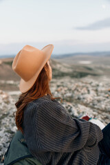 Wall Mural - Woman in hat contemplates sunset on rock overlooking vast landscape at dusk