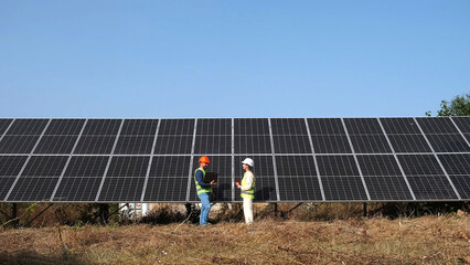 Wall Mural - A man and a woman in hard hats discuss work tasks near solar panels on the street. Female environmental engineer talking to investor. Green electricity concept.