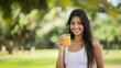 © Aamir - Indian woman smiling and holding glass of orange juice with blurred background, cheerful and refreshing, vibrant drink, happy expression